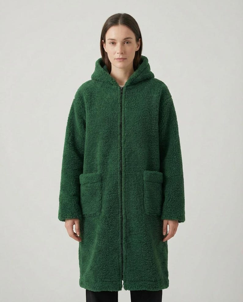 May include: A long-length, forest green hooded coat made of a textured, fuzzy fleece material. The coat features a full-length front zipper closure, long sleeves, and two large, rectangular patch pockets positioned on the front of the garment.