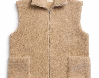 May include: A beige sleeveless vest made of textured sherpa fleece material. The garment features a full-length front zipper, a high collar, and two large square patch pockets on the lower front. A small white brand label is visible at the neck.