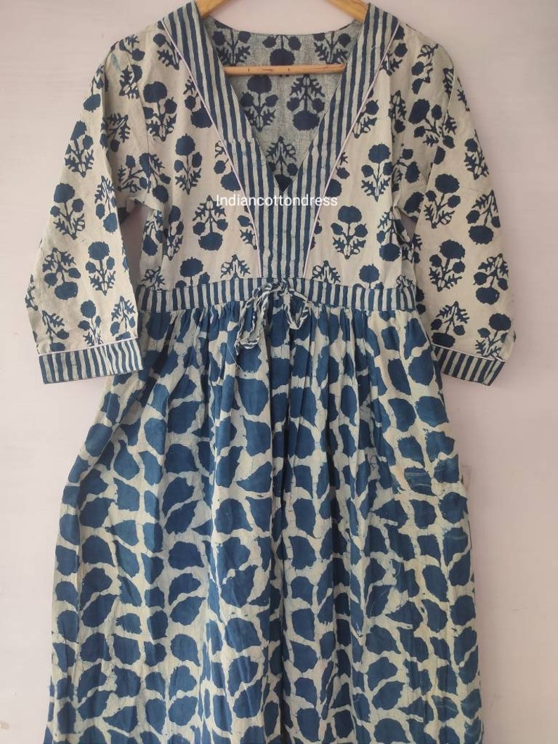 May include: A blue and white cotton dress with a V-neckline and 3/4 sleeves. The dress has a floral print on the top and a leaf print on the bottom. The dress has a tie at the waist.