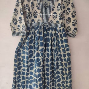May include: A long, loose-fitting dress with a V-neckline and 3/4 sleeves. The dress is made of a light-weight cotton fabric and features a blue and white floral print. The dress has a tie at the waist and a gathered skirt.