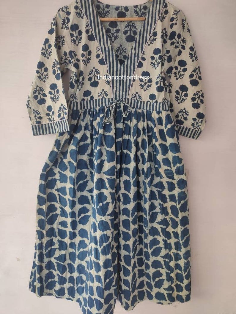 May include: A long, loose-fitting dress with a V-neckline and 3/4 sleeves. The dress is made of a light-weight cotton fabric and features a blue and white floral print. The dress has a tie at the waist and a gathered skirt.