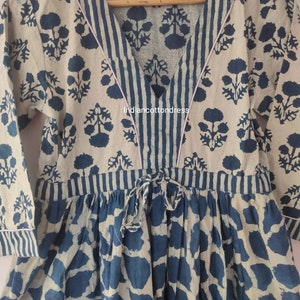 May include: A blue and white cotton tunic dress with a V-neckline, a tie at the waist, and a floral print. The dress has a striped trim around the neckline and sleeves.
