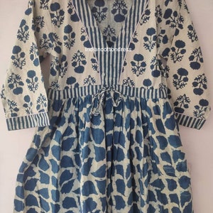 May include: A blue and white cotton dress with a V-neckline and a tie at the waist. The dress has a floral print on the top and a leaf print on the bottom. The dress is made in India. "Indiancottondress" is printed on the dress.
