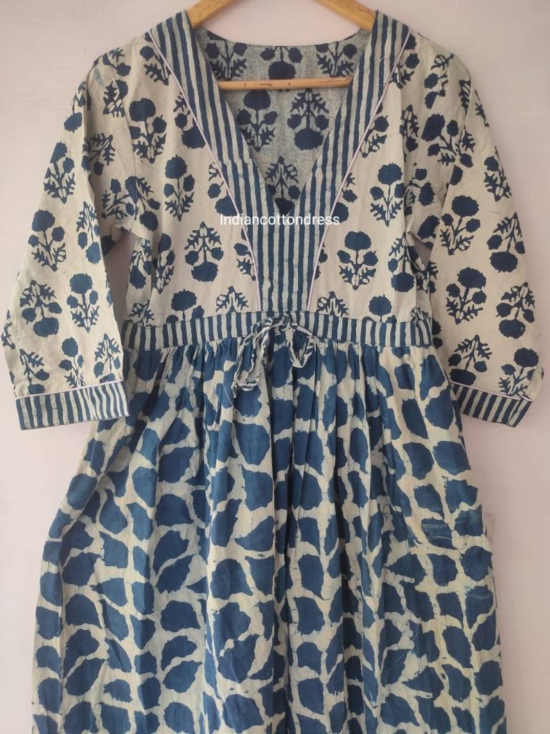 May include: A blue and white cotton dress with a V-neckline and a tie at the waist. The dress has a floral print on the top and a leaf print on the bottom. The dress is made in India. "Indiancottondress" is printed on the dress.