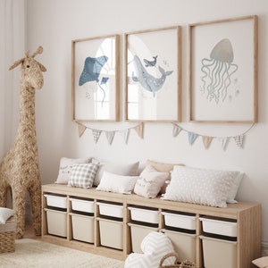 May include: A light wood shelf unit with six white storage bins. The shelf is decorated with a blue whale, a stingray, and a jellyfish, all in watercolor style. A blue and white patterned garland hangs above the shelf.