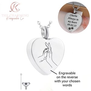 Peut inclure: Un collier pendentif argenté en forme de cœur avec un motif de patte et de main. Le pendentif est gravable au verso. L'image montre également un gros plan d'un pendentif en forme de cœur avec le texte "Charlie Always in my heart 09.02.23".