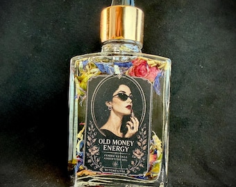 Op de afbeelding: Een doorzichtige glazen druppelfles met een gouden dop, gevuld met olie en gedroogde kleurrijke bloemblaadjes. Het etiket bevat een illustratie van een persoon met een zonnebril en lippenstift, met de tekst OLD MONEY ENERGY FEMME FATALE ANOINTING OIL WITCHELIXIR.