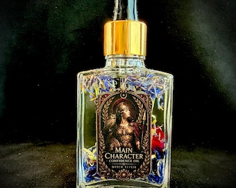 Op de afbeelding: Een doorzichtige glazen druppelfles gevuld met vloeistof en gedroogde blauwe en rode bloemblaadjes. Het etiket bevat een illustratie van een krijger met een uil en de tekst MAIN CHARACTER CONFIDENCE OIL WITCH ELIXIR in goud en zwart.