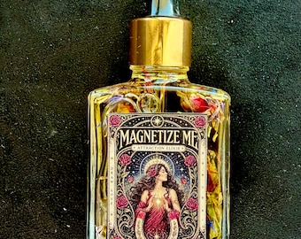 Op de afbeelding: Een doorzichtige glazen druppelfles gevuld met gele olie en gedroogde bloemblaadjes. Het etiket bevat de tekst "MAGNETIZE ME", "ATTRACTION ELIXIR", "DRAW LOVE" en "RITUAL OIL" met een illustratie van een persoon omringd door rozen.