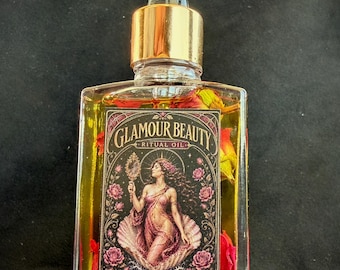Op de afbeelding: Een doorzichtige glazen fles gevuld met goudkleurige olie en gedroogde bloemblaadjes, afgesloten met een goudkleurige druppeldop. Het rechthoekige etiket bevat de tekst GLAMOUR BEAUTY RITUAL OIL en een afbeelding van een figuur met een handspiegel.