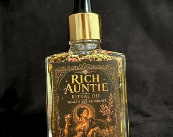 May include: A clear glass dropper bottle filled with yellow oil and dried botanicals. The black label features gold text reading Rich Auntie Ritual Oil Wealth and Abundance Witch Elixir and an illustration of a person holding a goblet.