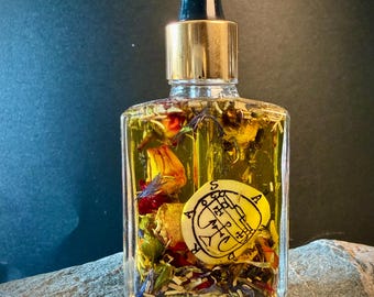 May include: A clear glass bottle filled with yellow liquid and dried flowers, topped with a gold and black dropper. A round, yellow emblem with black symbols is visible inside the bottle. The bottle sits on a gray stone surface.