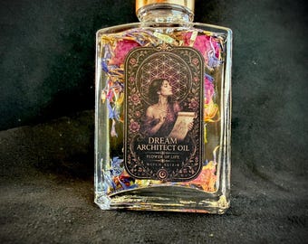 Op de afbeelding: Een doorzichtige glazen fles gevuld met vloeistof en gedroogde bloemblaadjes in roze, blauwe en gele tinten. Het etiket bevat een illustratie van een persoon met een rol, de tekst DREAM ARCHITECT OIL, FLOWER OF LIFE en WITCH ELIXIR.