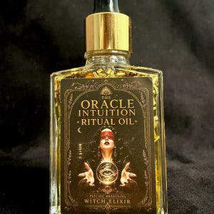 May include: A clear glass bottle with a gold dropper cap containing yellow oil and gold flakes. The black label features the text THE ORACLE INTUITION RITUAL OIL, PSYCHIC AWAKENING, and WITCH ELIXIR, with an illustration of a person holding a crystal ball.