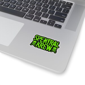 May include: A green and black sticker with the text "SPEKTRAL KREW" in a bold, stylized font. Two skull and crossbones graphics flank the text.