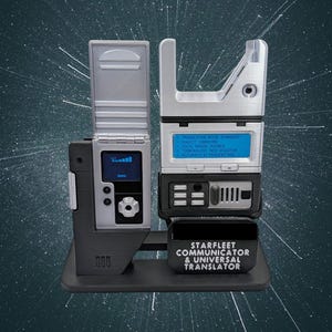 May include: A Starfleet Communicator and Universal Translator prop. The device is mainly silver and black, with a small screen displaying blue text. The base has the text "STARFLEET COMMUNICATOR & UNIVERSAL TRANSLATOR".