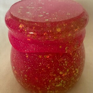 May include: A pink glass jar with a lid, decorated with gold and white glitter.
