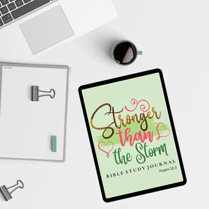 Puede incluir: Un diario verde y blanco con el texto "Stronger than the Storm" en letras doradas y rosas. El diario también incluye el texto "Bible Study Journal" y "Psalm 31:3".