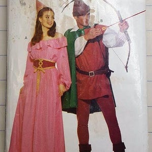 May include: A vintage Butterick sewing pattern envelope featuring illustrations of two medieval costumes. One is a pink dress with a gold belt, and the other is a red tunic and pants with a green cape. The envelope has the text "BUTTERICK" and "5749".