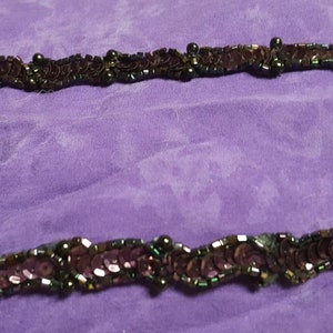 May include: A close-up of a dark green and purple beaded trim with a wavy pattern. The trim is made of sequins and beads.