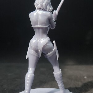 May include: A 3D printed figurine of a female figure holding a sword. The figure is wearing a detailed outfit with a skirt and boots. The figurine is painted in a light gray color.