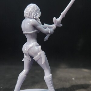 May include: A gray 3D printed figurine of a female warrior holding a sword. The figurine is standing on a round base.