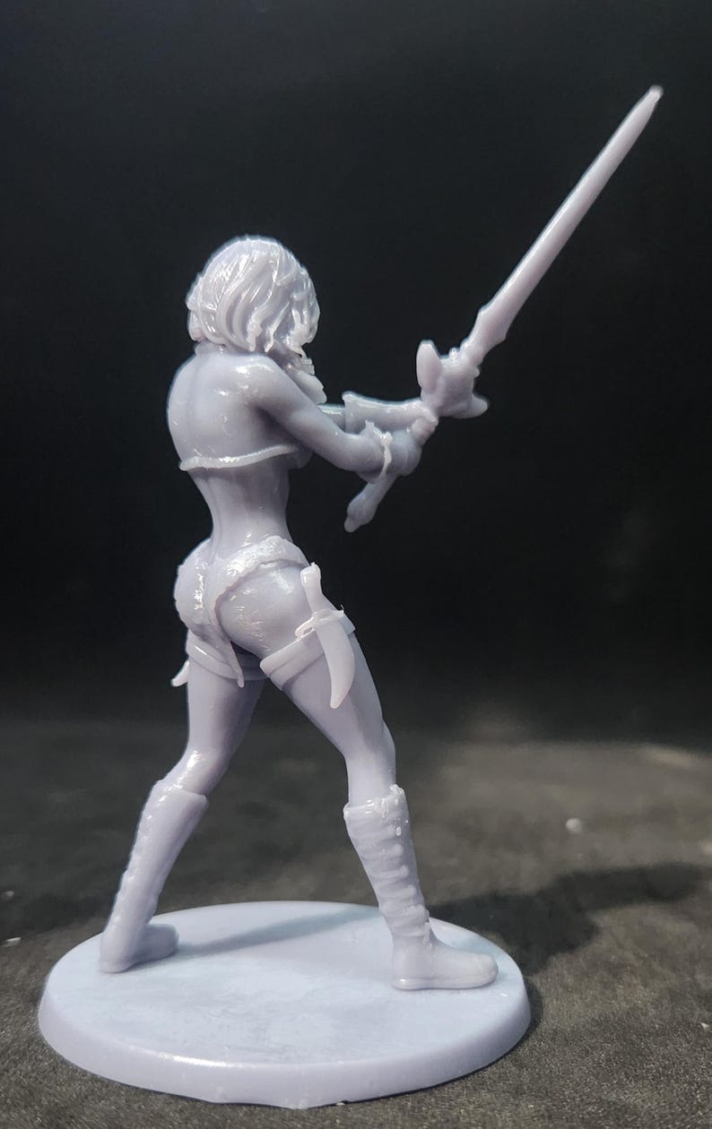 May include: A gray 3D printed figurine of a female warrior holding a sword. The figurine is standing on a round base.