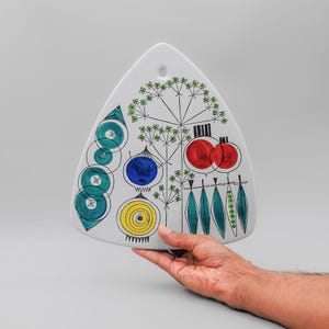 May include: A white, triangular ceramic serving platter with a hand-painted design. The design includes teal circles, a blue onion, yellow spiral, red fruits, and green leaves. The platter has a hole for hanging.