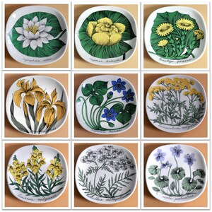 May include: Nine white ceramic plates with floral designs. Each plate features a different flower or plant, including a water lily, a yellow flower, a dandelion, an iris, a blue flower, a yellow flower, a yellow flower, a white flower, and a purple flower. The plates are all square and have a white background.