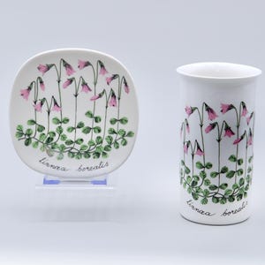 May include: A white ceramic mug and saucer with a floral design. The design features pink flowers and green leaves with the text "linnaea borealis" on both pieces.