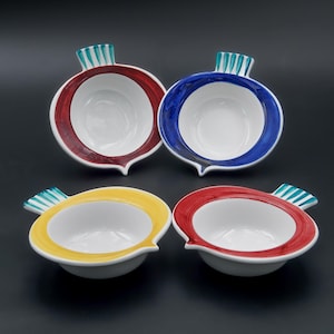 Puede incluir: Cuatro cuencos de cerámica con forma de rábano, cada uno con interior blanco y borde de color. Dos cuencos tienen bordes rojos, uno tiene borde azul y otro borde amarillo. Cada cuenco tiene un asa a rayas verdes y blancas.