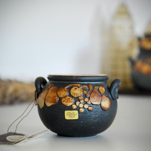 May include: A small black ceramic pot with brown fruit designs and a gold label that reads "Hand Made in Portugal".