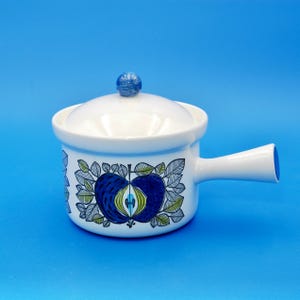 May include: White ceramic pot with a lid and a handle. The pot has a blue and green apple design with leaves.
