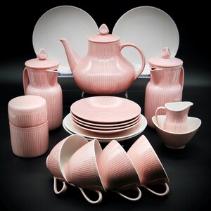 Könnte beinhalten: Ein rosafarbenes Teeservice mit Teekanne, Milchkännchen, Zuckerdose, Tassen, Untertassen und einem Serviertablett. Das Set hat ein geripptes Design und ist aus Porzellan.