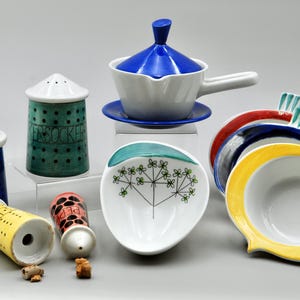May include: A set of nine ceramic kitchenware items in various colors and patterns. The set includes a blue and white gravy boat, a green and white bowl with a stylized plant design, a yellow bowl with a red rim, and several salt and pepper shakers.