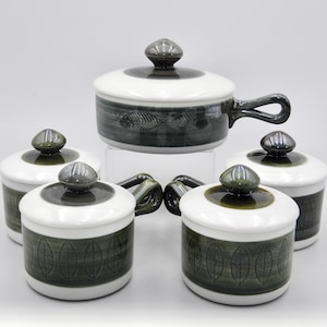 Puede incluir: Conjunto de cinco ramequines de cerámica blanca con diseños de hojas verdes y tapas a juego. Los ramequines tienen una forma redondeada y una pequeña asa en el lateral.