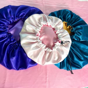 K&ouml;nnte beinhalten: Drei Hauben aus Satin in den Farben Violett, Hellrosa und Petrol. Jede Haube hat einen gerafften, elastischen Rand mit einer glatten, gl&auml;nzenden Oberfl&auml;che. Die petrolfarbene Haube verf&uuml;gt &uuml;ber einen schwarzen, verstellbaren Kordelzug.