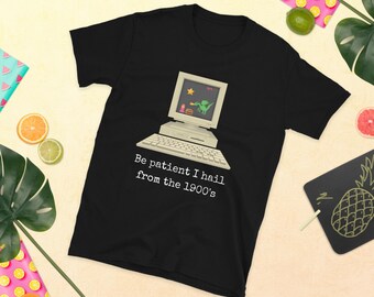 Puede incluir: Camiseta negra con un gráfico de computadora vintage blanco y el texto "Be patient I hail from the 1900's".