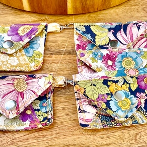 May include: Four floral fabric pouches with snap closures and attached key rings. The pouches are made of different floral patterns in shades of pink, blue, yellow, and green.