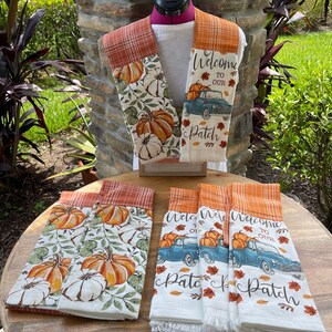 May include: Set of six kitchen towels with a fall theme. The towels feature a vintage truck with pumpkins, fall leaves, and the text "Welcome to our Patch". The towels are white with orange and brown plaid trim.