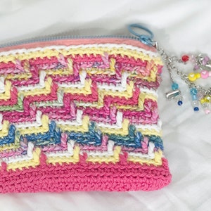 May include: A pink crocheted zippered pouch with a colorful beaded charm attached. The pouch has a white, yellow, blue, and pink striped pattern.
