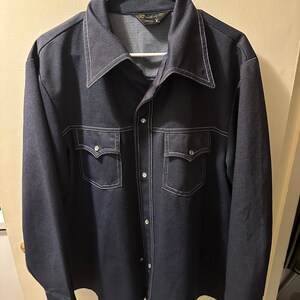 May include: A dark blue long-sleeved button-up shirt with white stitching detail. The shirt has two chest pockets with button closures and a pointed collar.