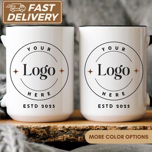 May include: Two white ceramic mugs with black handles and rims. Each mug features a circular logo design with the text "YOUR Logo HERE" and "ESTD 2025". The image also includes a "FAST DELIVERY" banner.