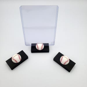 May include: Three black baseball-themed display stands with a clear acrylic sign holder. Each stand features a white baseball with red stitching.