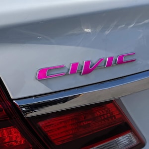 May include: A white car with a pink "CIVIC" emblem on the back.