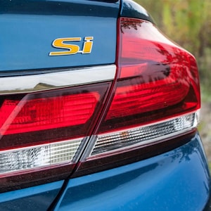 May include: A blue car with a red taillight and a yellow "Si" emblem on the trunk.