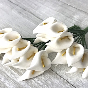 May include: A bunch of white artificial calla lilies with yellow centers. The stems are green and wired.