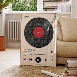 May include: A framed print featuring a vinyl record design with a red center and black grooves. The print includes a music player interface with song information and playback controls. The artwork is displayed in a bright, airy room with a plant and wooden furniture.