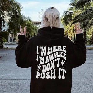 May include: Black hooded sweatshirt with white text that reads "I'm here I'm awake Don't push it" with lightning bolt symbols on either side of the word "Don't".
