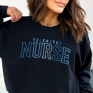 May include: Black sweatshirt with a blue and white gradient graphic that says "Telemetry Nurse".